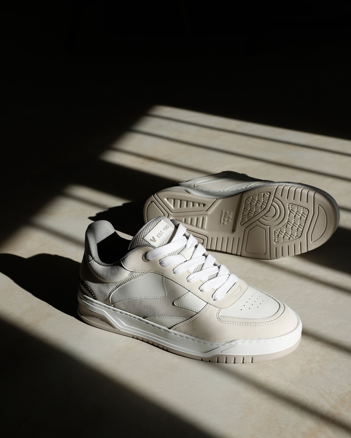 Foto van beige VIA VAI heren sneakers Jay Randy, op betonnen vloer in zonlicht.