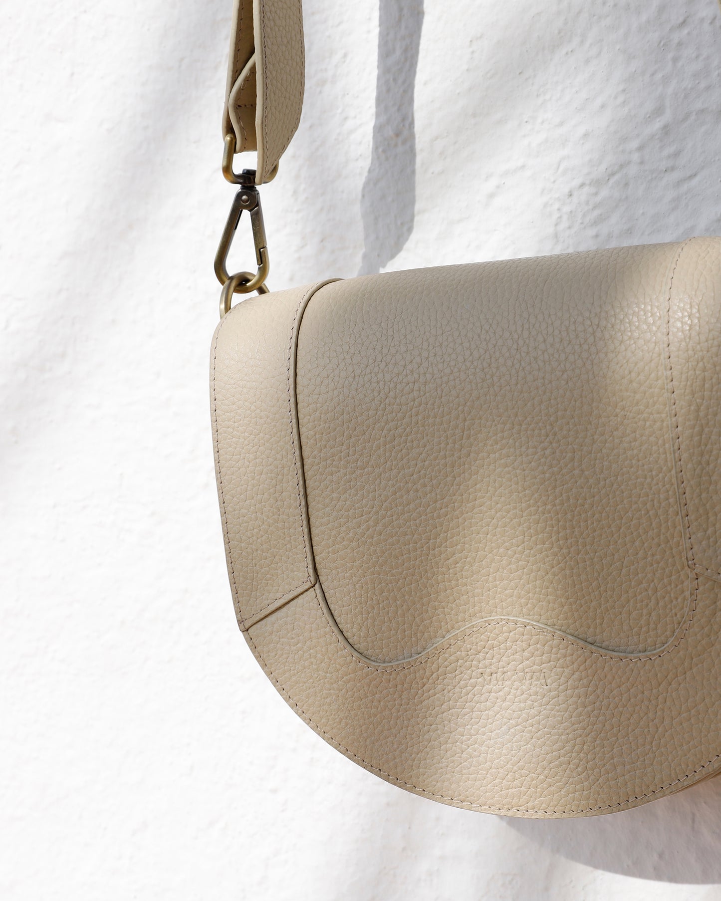 Detailfoto van VIA VAI beige leren schoudertas dames Mae Lizzy, hangend voor witte muur.