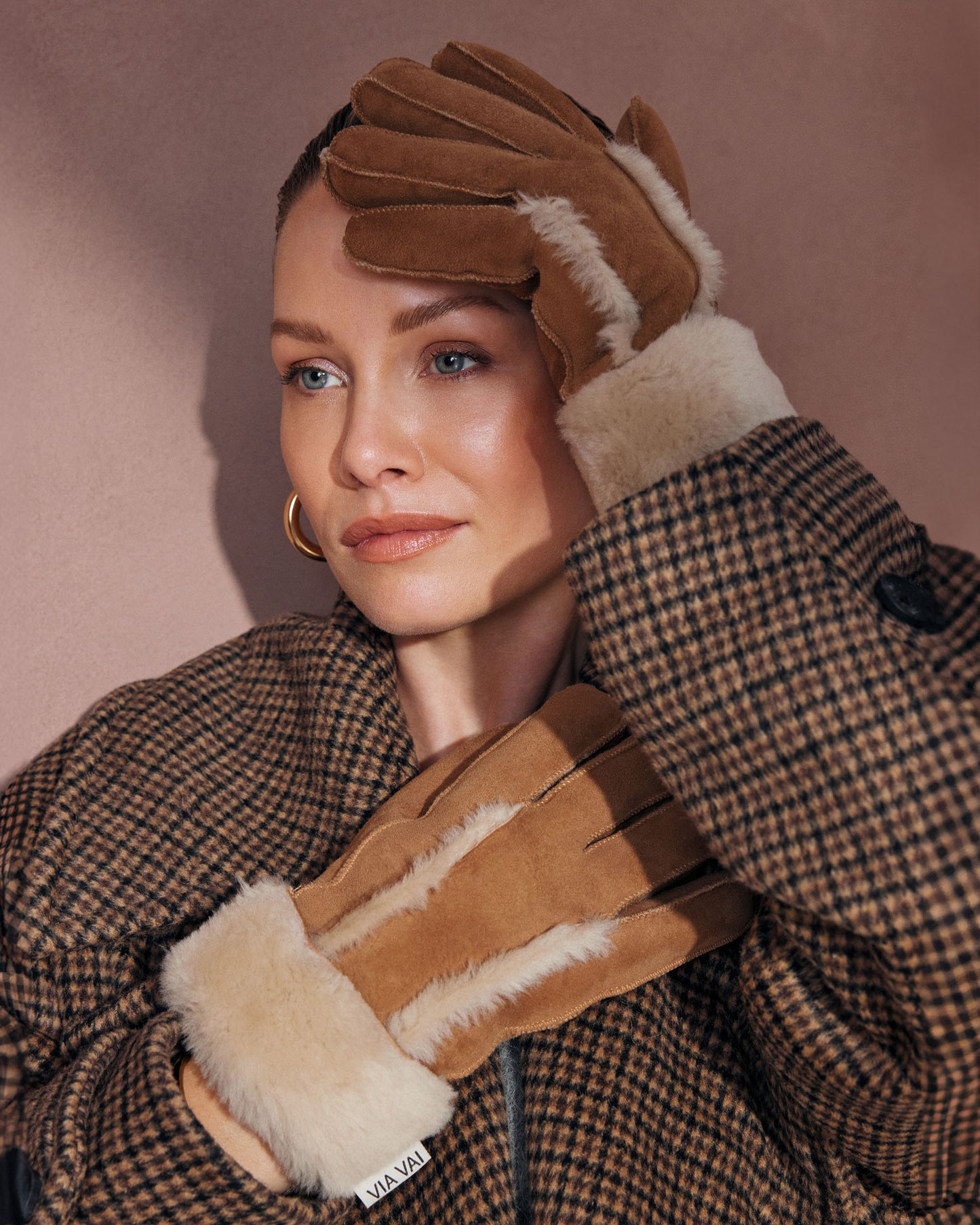 Woman wearing brown gloves with fur lining, posing against a neutral background